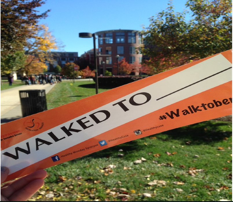 Walktober bumper sticker being held in front of a scene of the SU Shaw Quadrangle