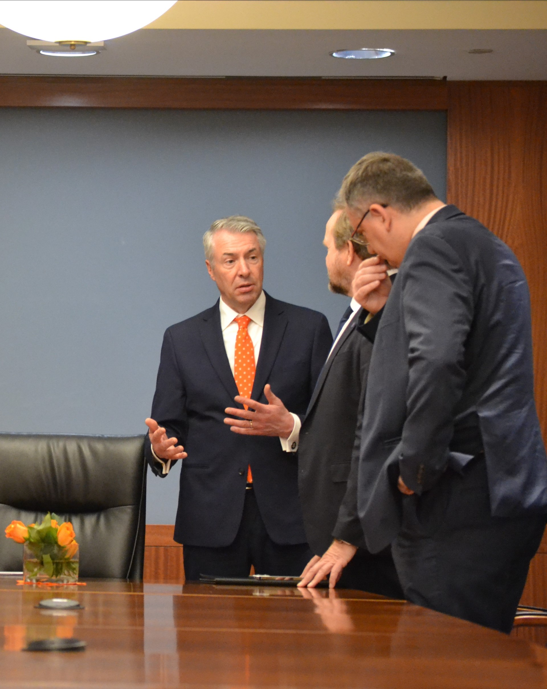 Three men standing near a meeting table.