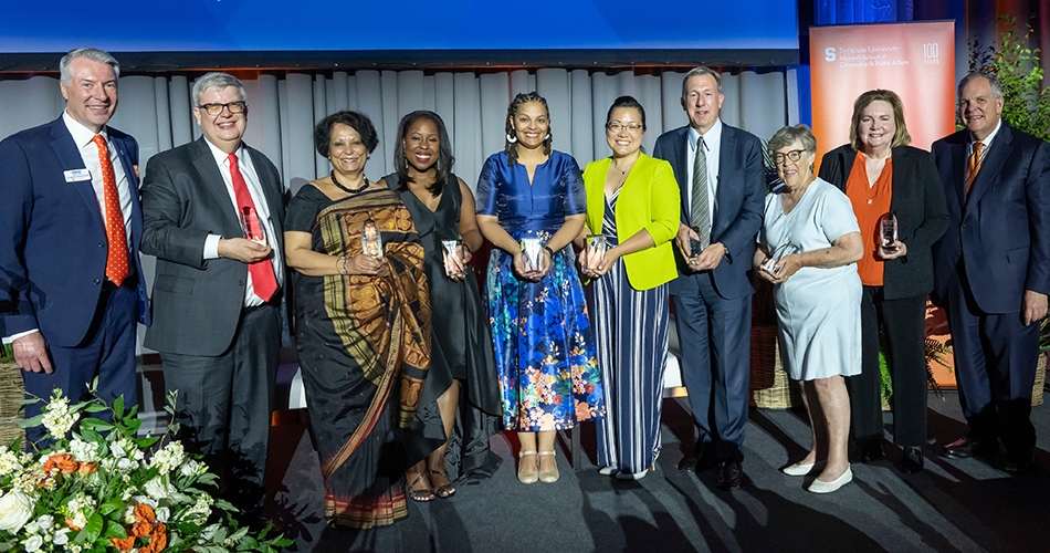 Group of people posing on a stage holding awards