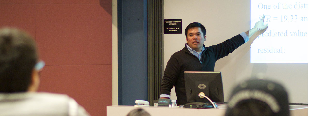 Professor teaching in front of a classroom pointing at the screen