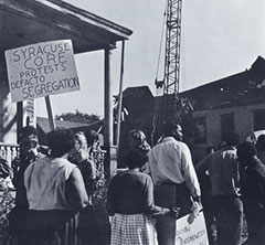 African-American demonstraters marching and holding signs, one of which says, 