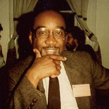 Portrait of a man who is wearing a suit and has glasses, with his hand on his chin