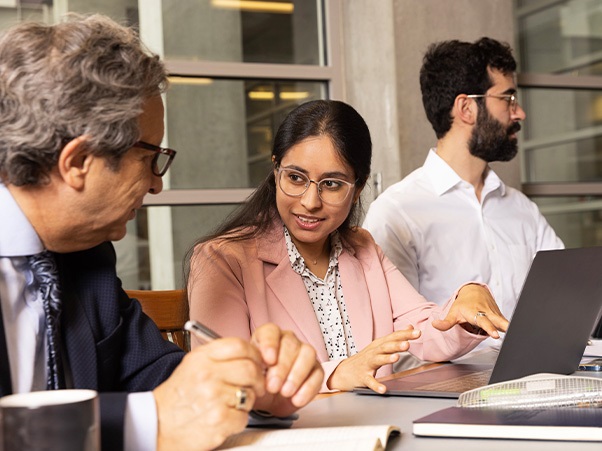 Three people sitting at a table, two of them talking to each other